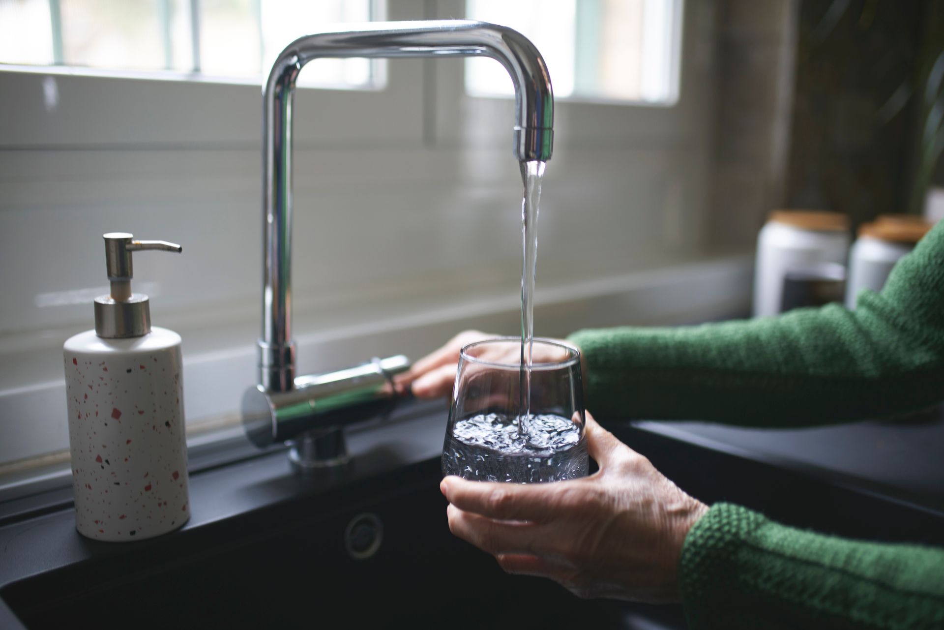 Close-up of clean water pouring into glass from faucet with well water filtration system.