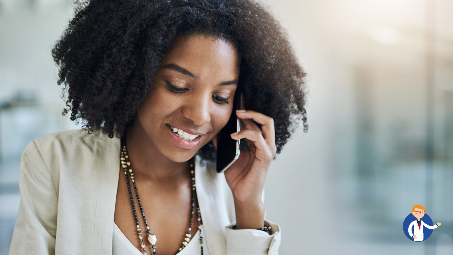Woman smiling, talking on a smartphone indoors, wearing a white jacket and necklace.