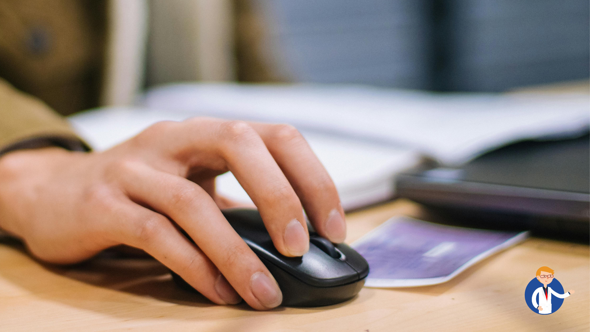 Person's hand on a computer mouse. Notebook and a card are nearby.