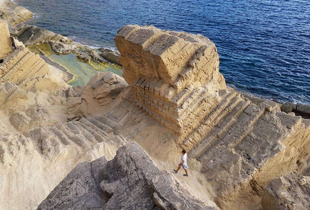 Person walking on eroded sandstone cliffs near the ocean.