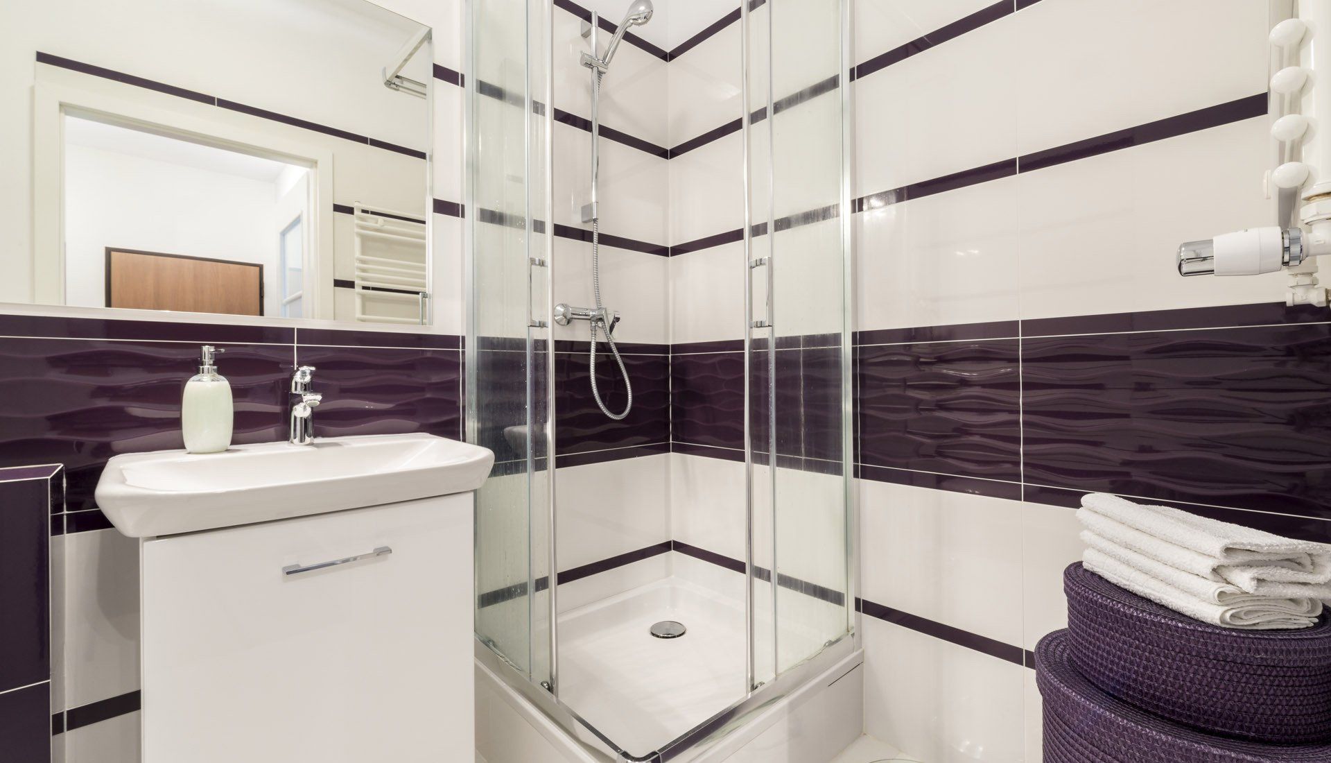 A bathroom with purple and white tiles and a walk in shower.