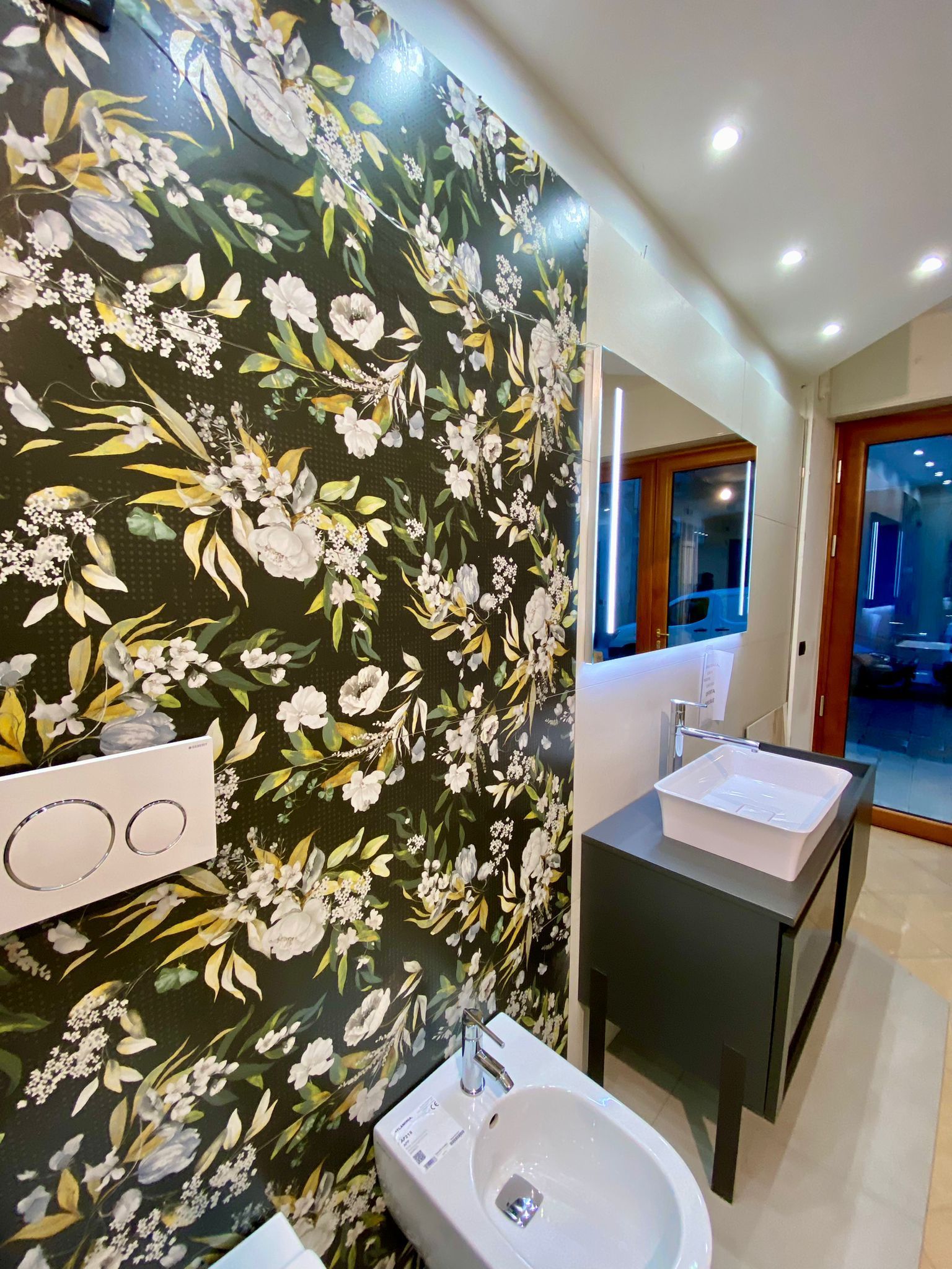 Un bagno con lavabo, wc, specchio e carta da parati floreale.