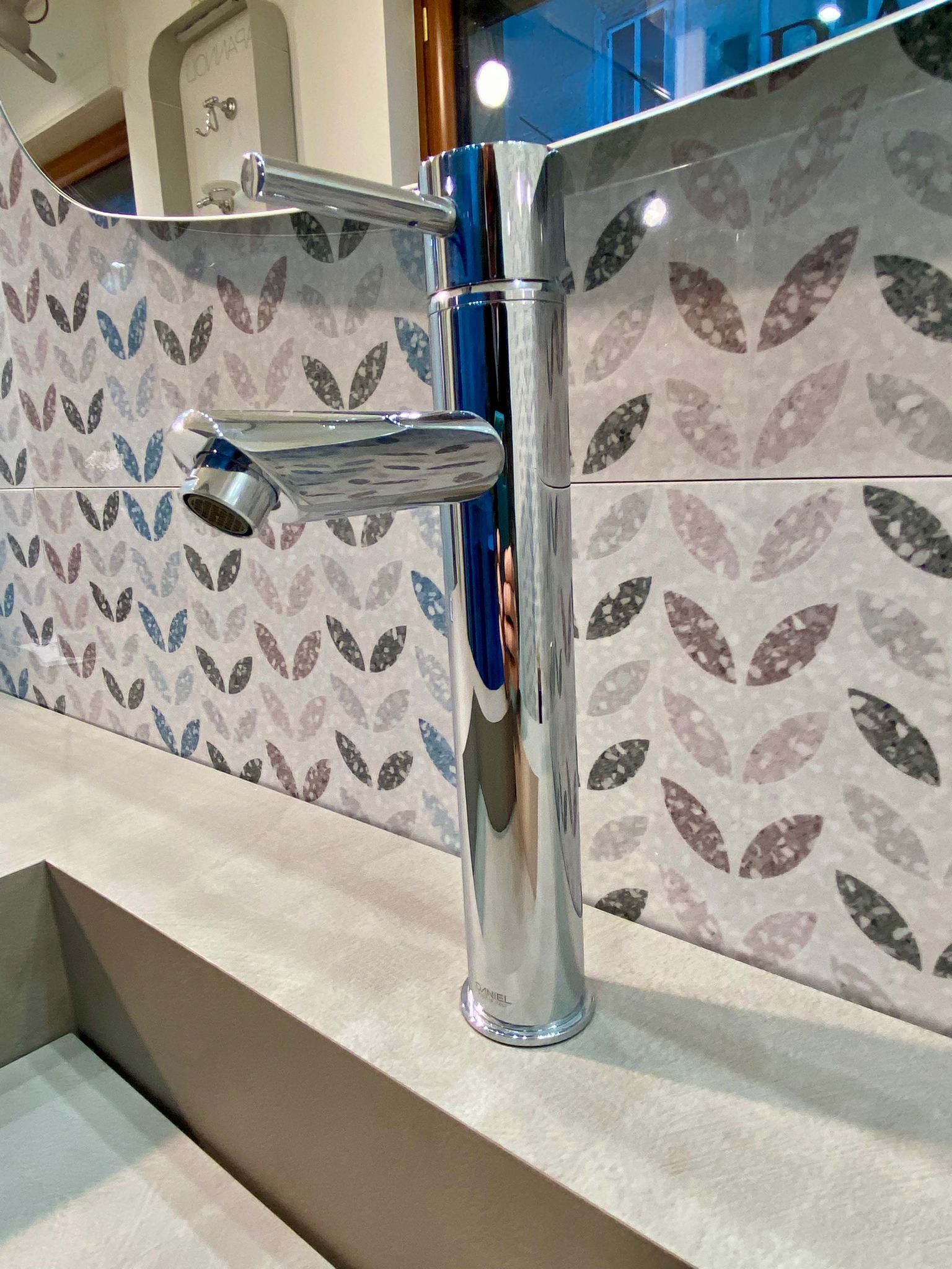 Un lavandino del bagno con un rubinetto e un muro piastrellato con foglie sopra.