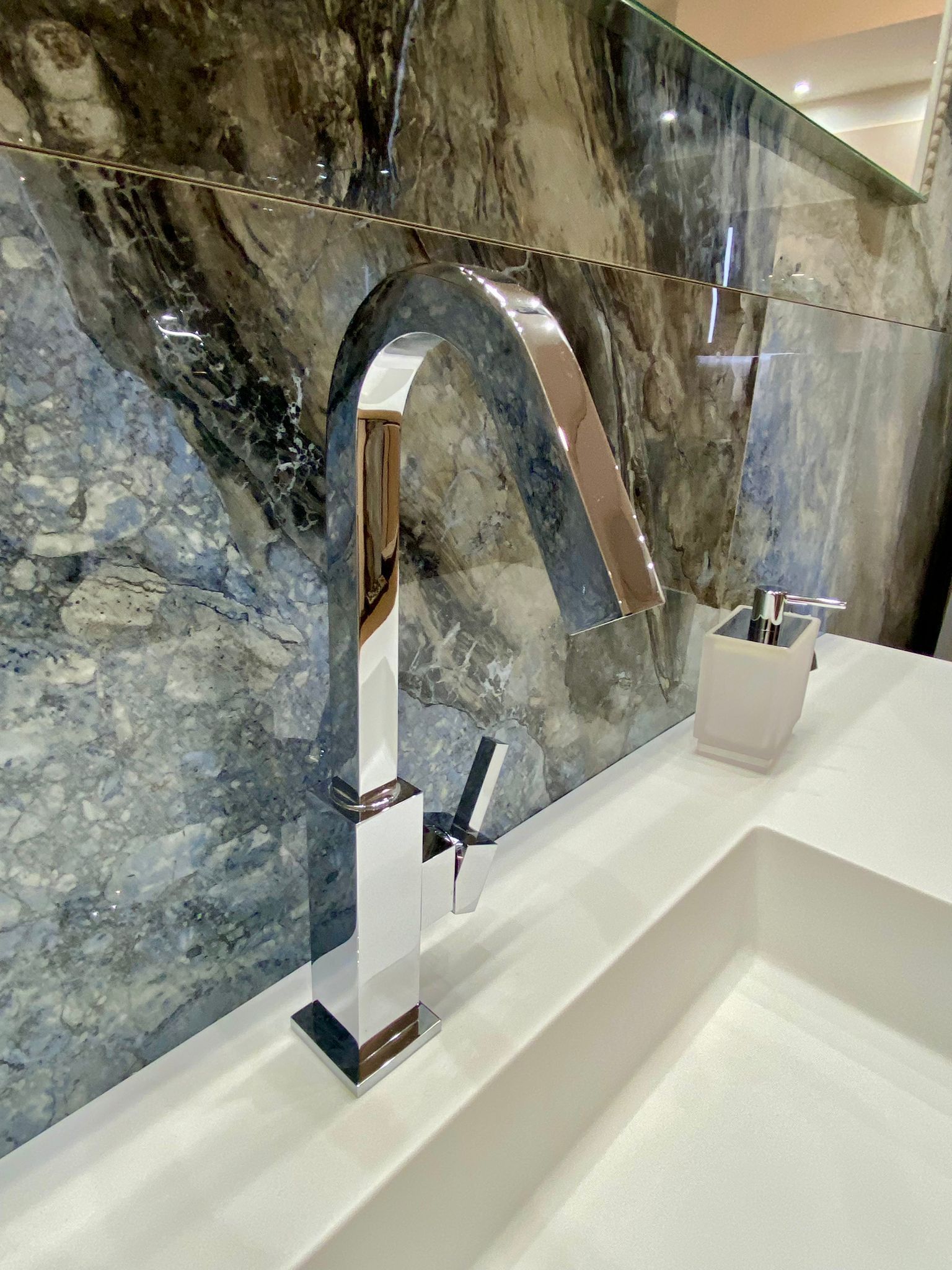 Un lavandino del bagno con rubinetto cromato e dispenser per sapone.