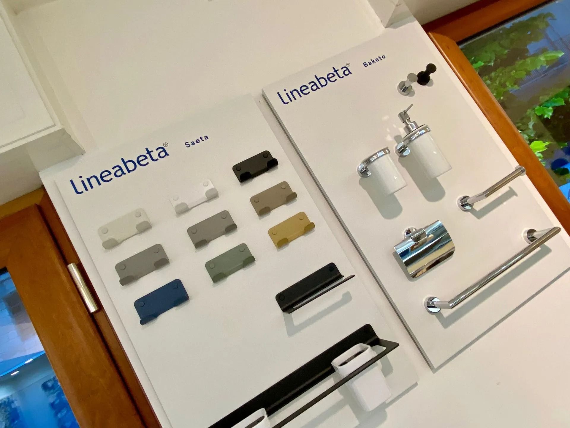 Esposizione di accessori per il bagno con portasciugamani, ganci e accessori a parete su pannelli bianchi.