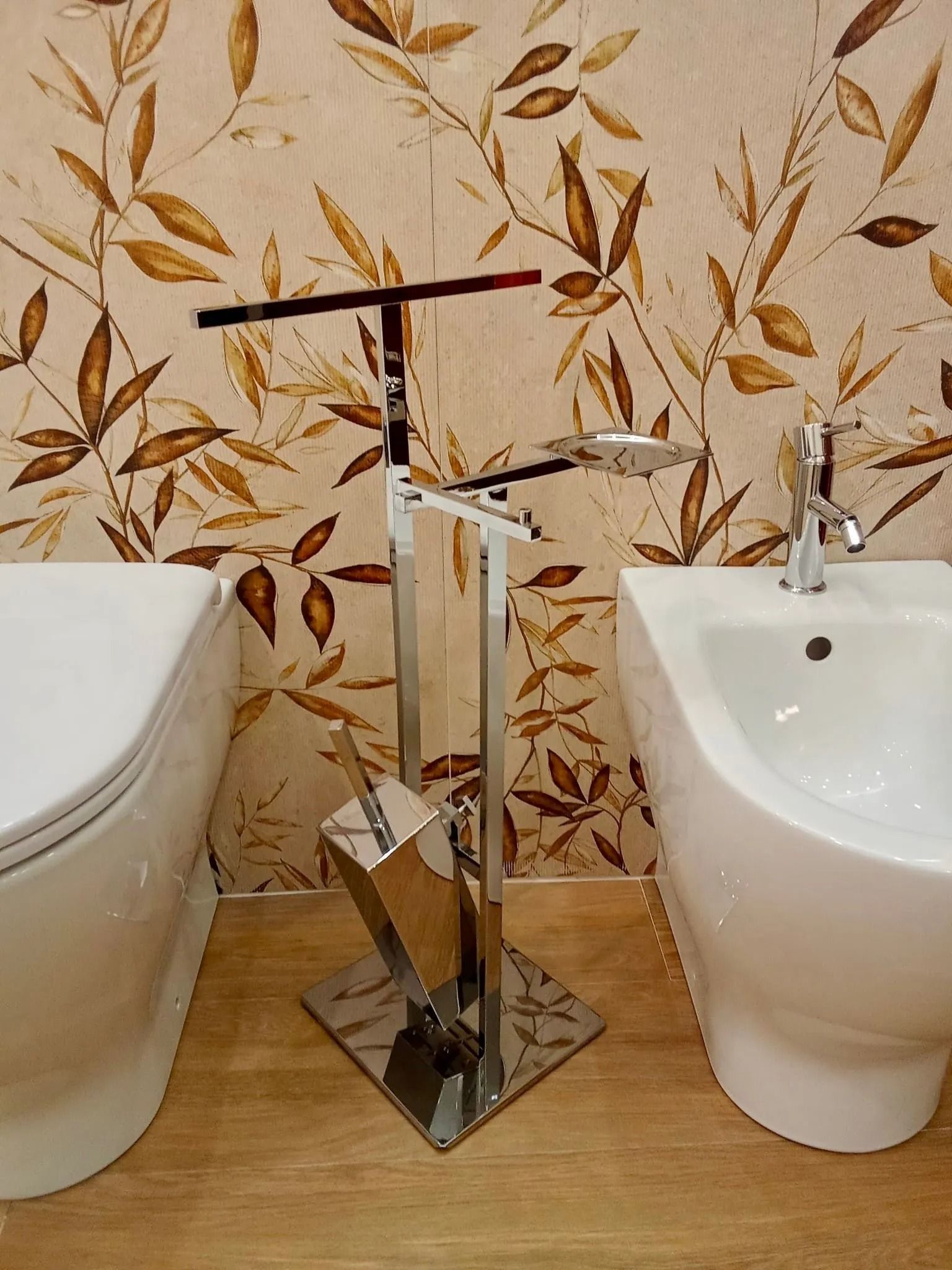 Supporto cromato tra WC e bidet in un bagno con carta da parati floreale.