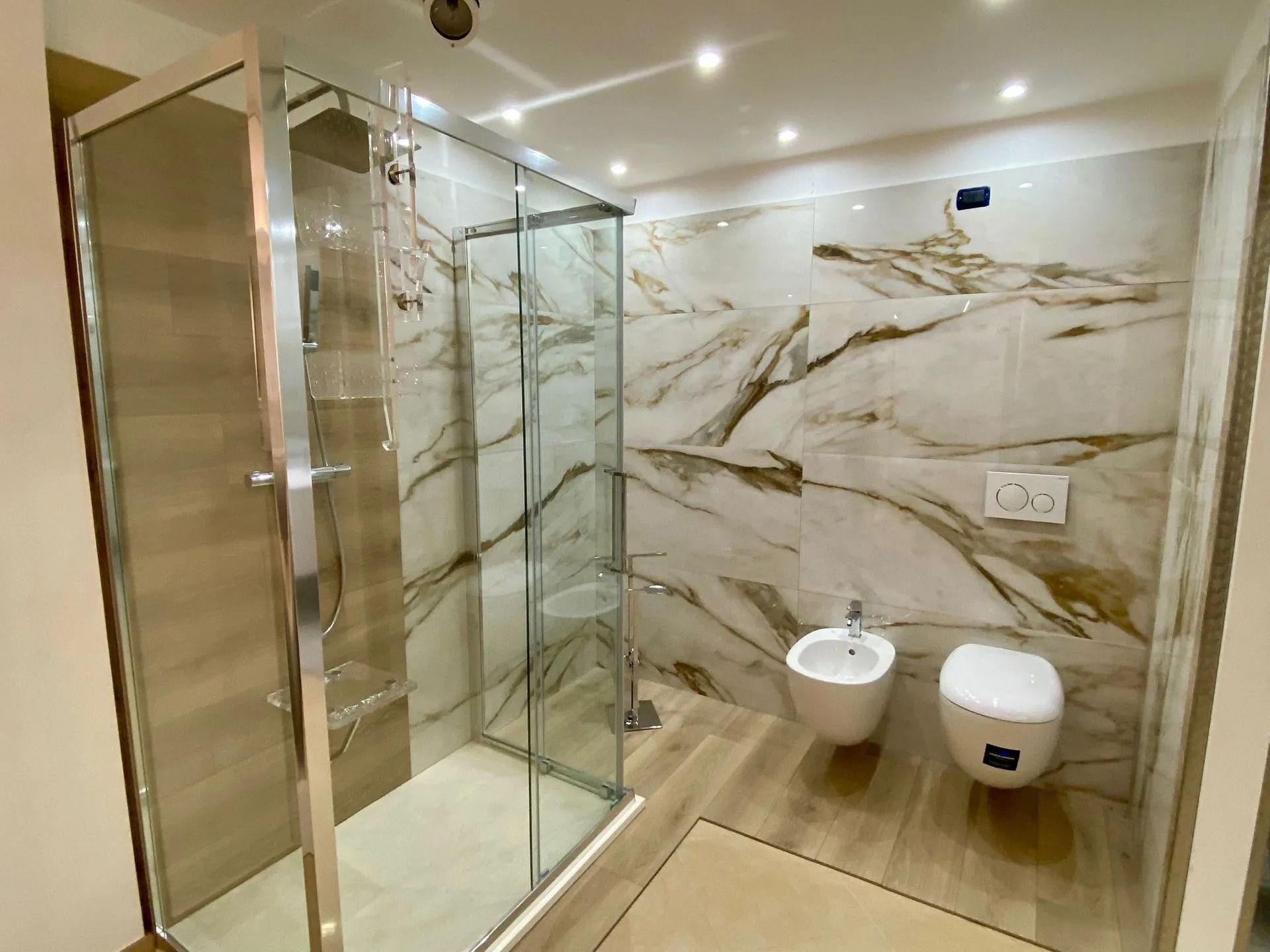 Bagno moderno con doccia in vetro, pareti in marmo, WC sospeso e rubinetteria bidet.