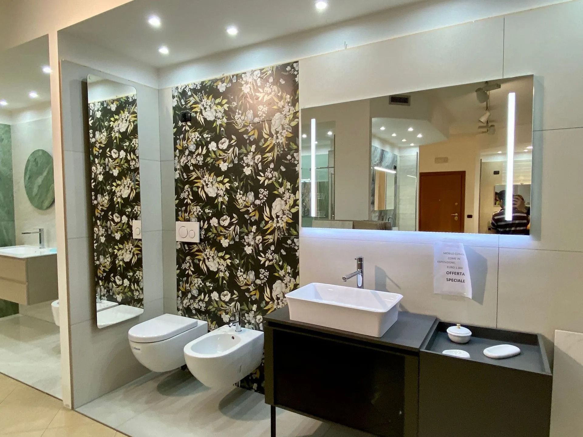 Bagno moderno con parete decorata con motivi floreali, lavabi a parete, specchi e sanitari bianchi.