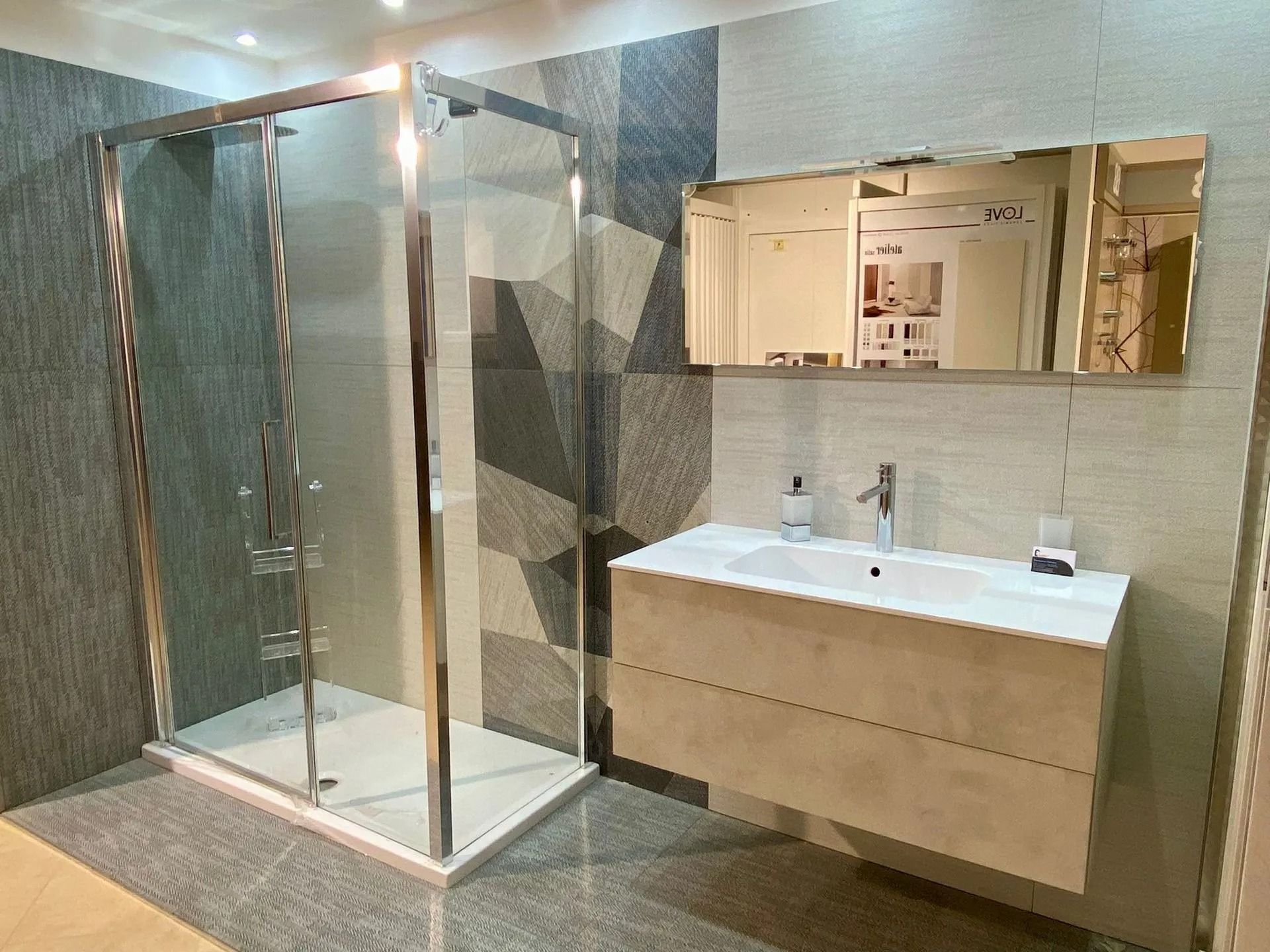 Bagno moderno con box doccia in vetro, lavabo con mobiletto, specchio e pareti rivestite con piastrelle neutre.