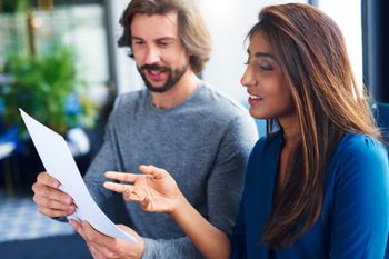 Two coworkers reviewing a document outdoors, one pointing at the page