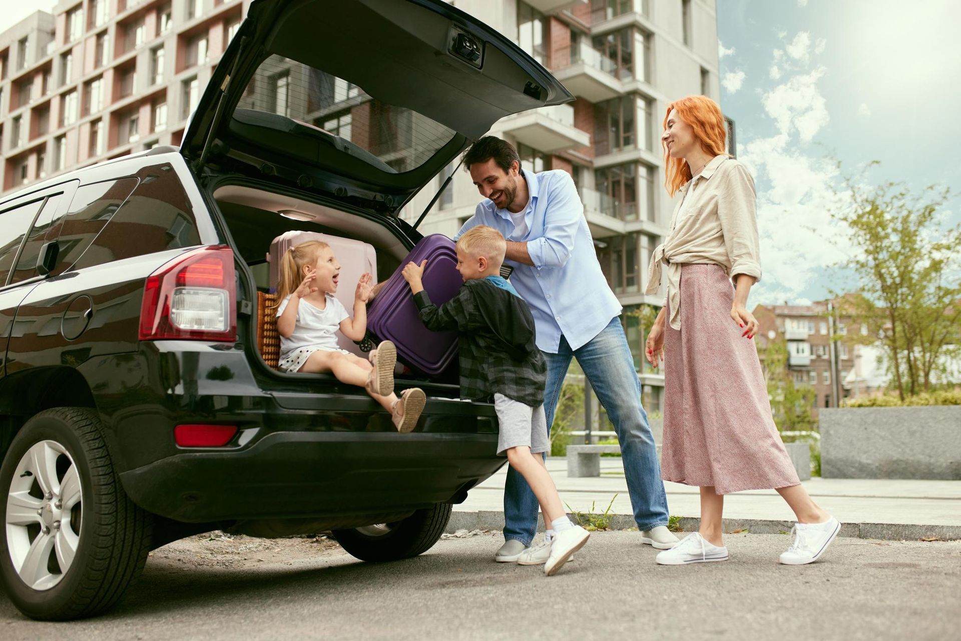 Family unloading luggage from open SUV in a parking lot