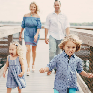 Family walking on a boardwalk, with two children in front and two adults behind, on a sunny day