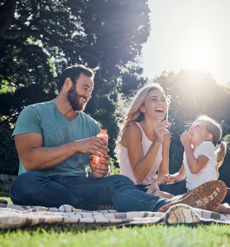 Family sitting on a picnic blanket in a sunny park, laughing and enjoying drinks together