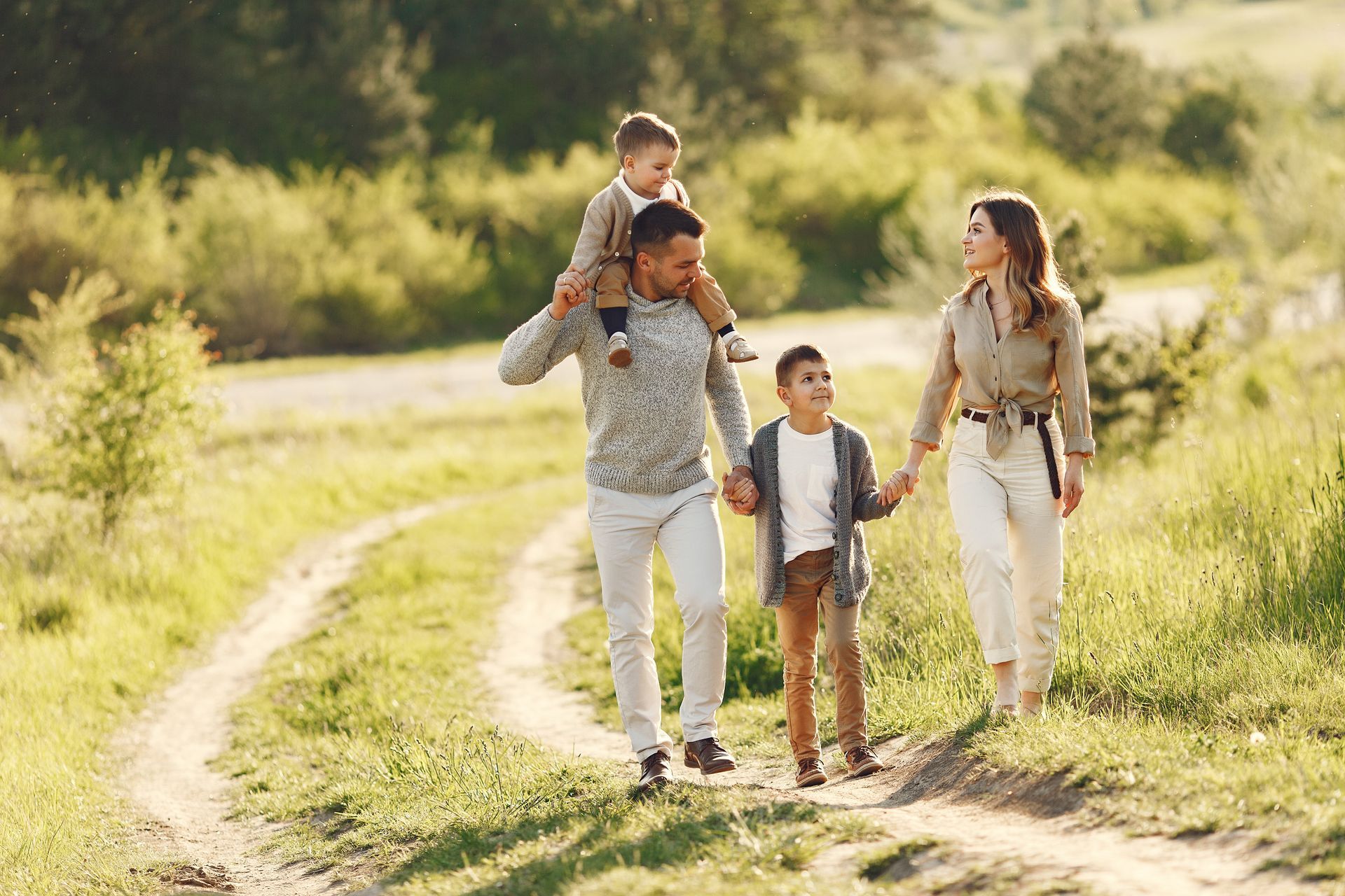 Family running barefoot along a sunny beach at low tide, smiling and splashing water