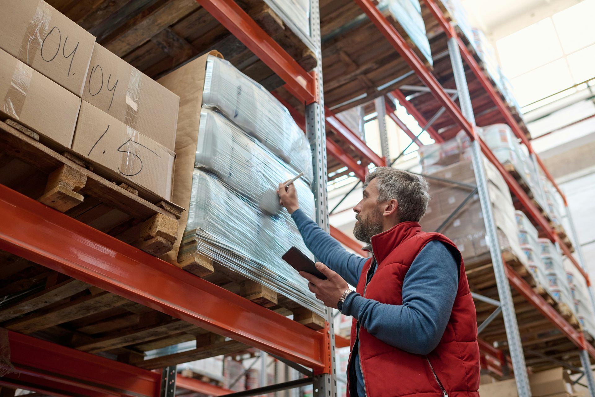 Worker in red vest reaching for a package on warehouse shelves
