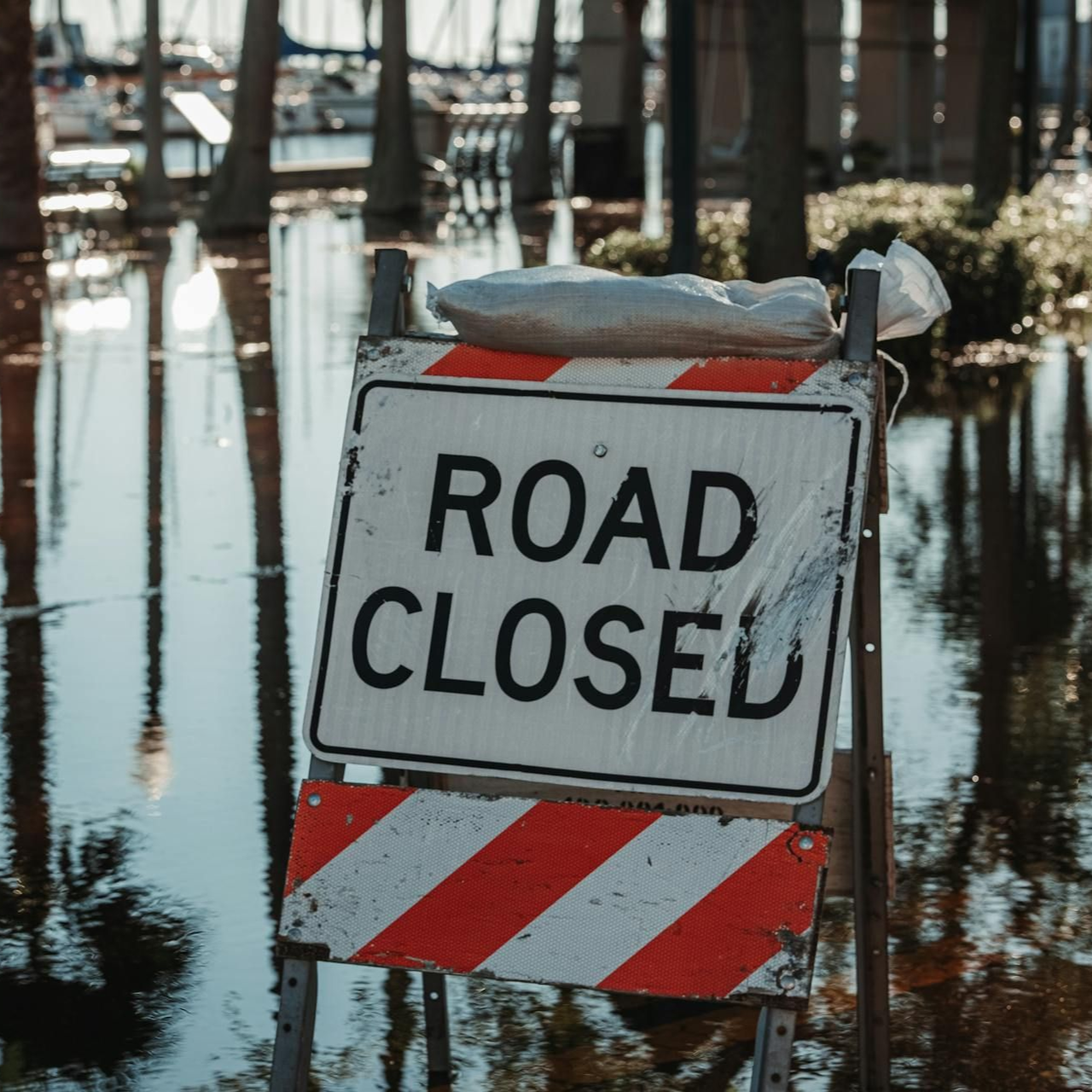 Road closed sign with red-and-white stripes beside flooded street reflections