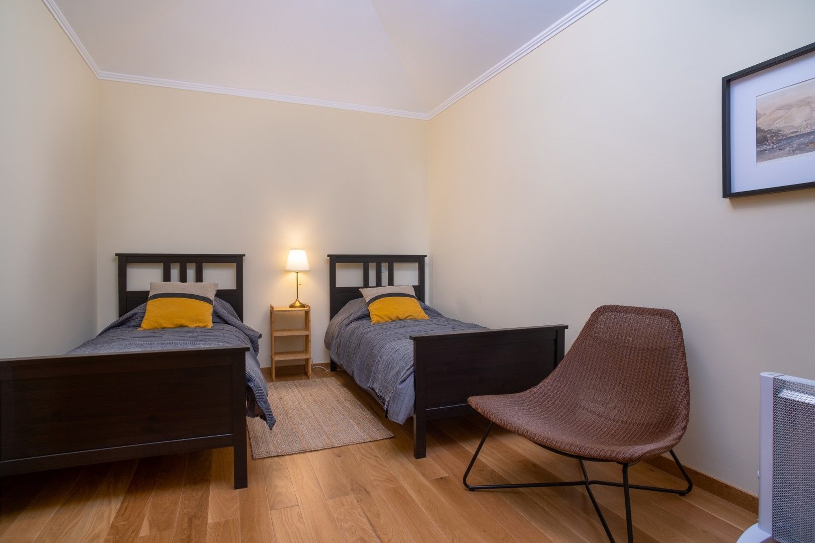 Bedroom with two twin beds, a chair, and a lamp. The walls are pale yellow, and the floor is hardwood.