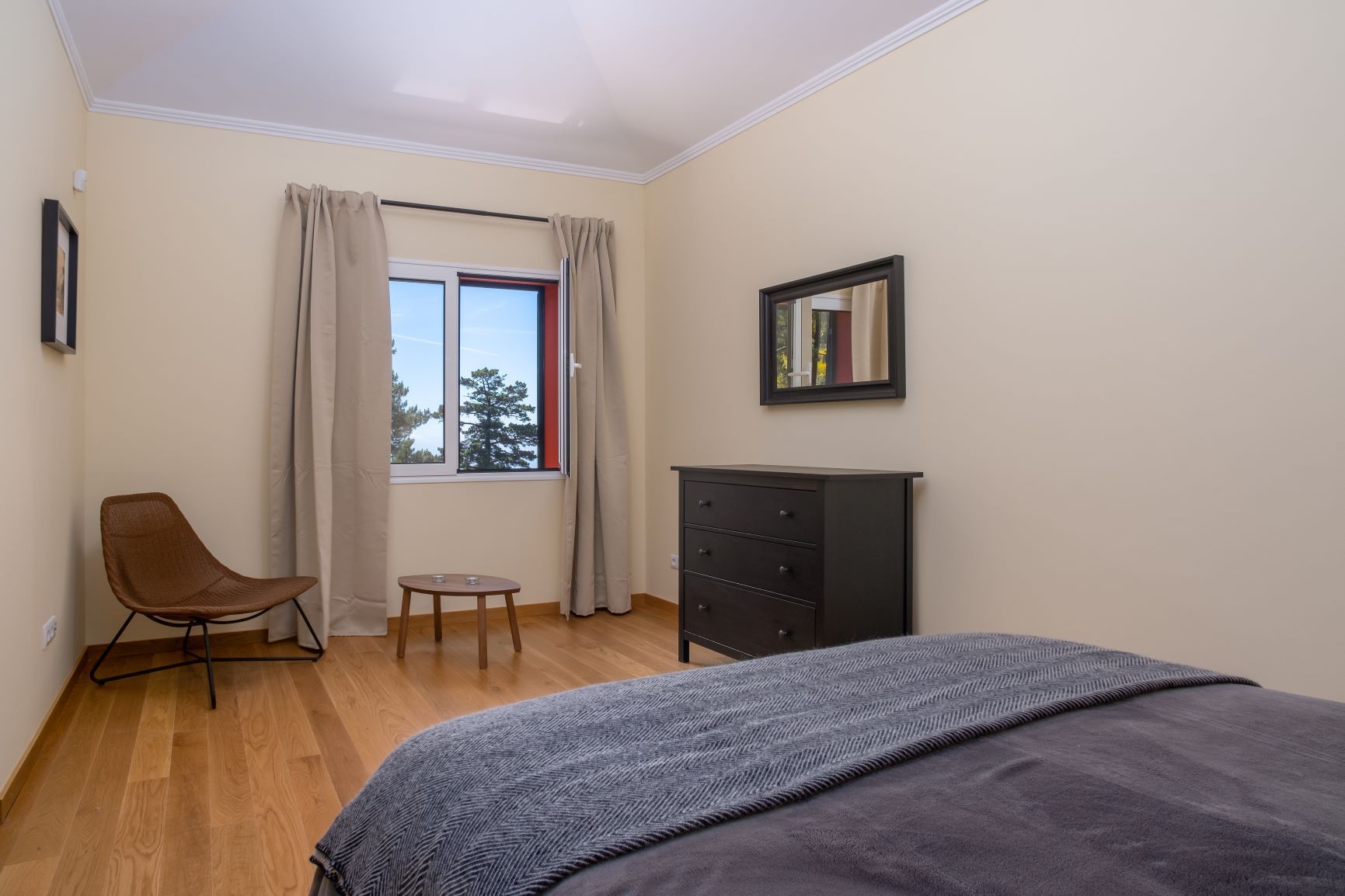 Bedroom with wood floor, bed, black dresser, chair, and window with curtains.