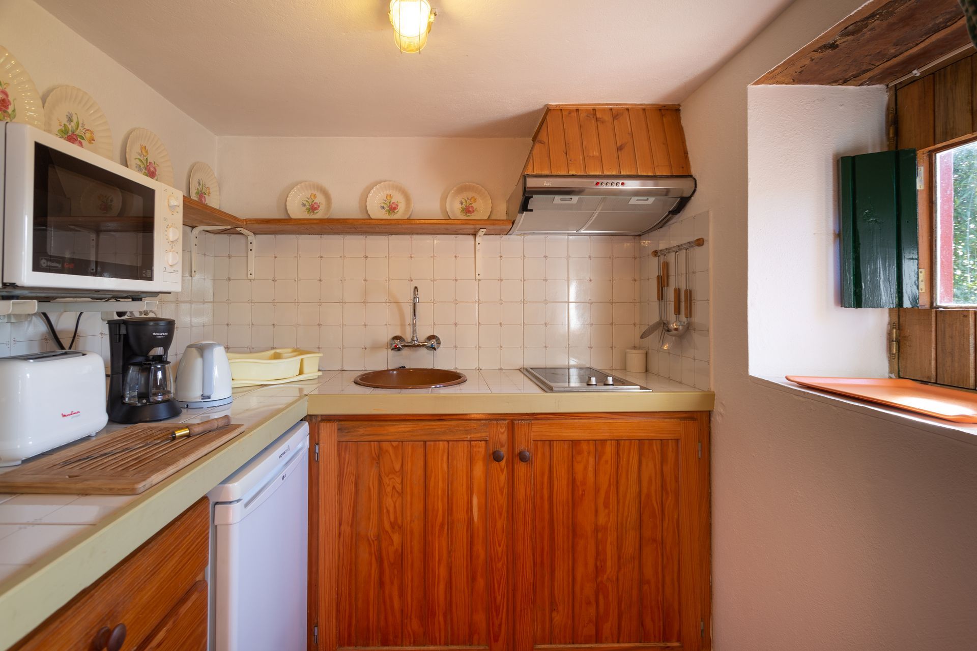 Small kitchen with wooden cabinets, appliances, and a window.