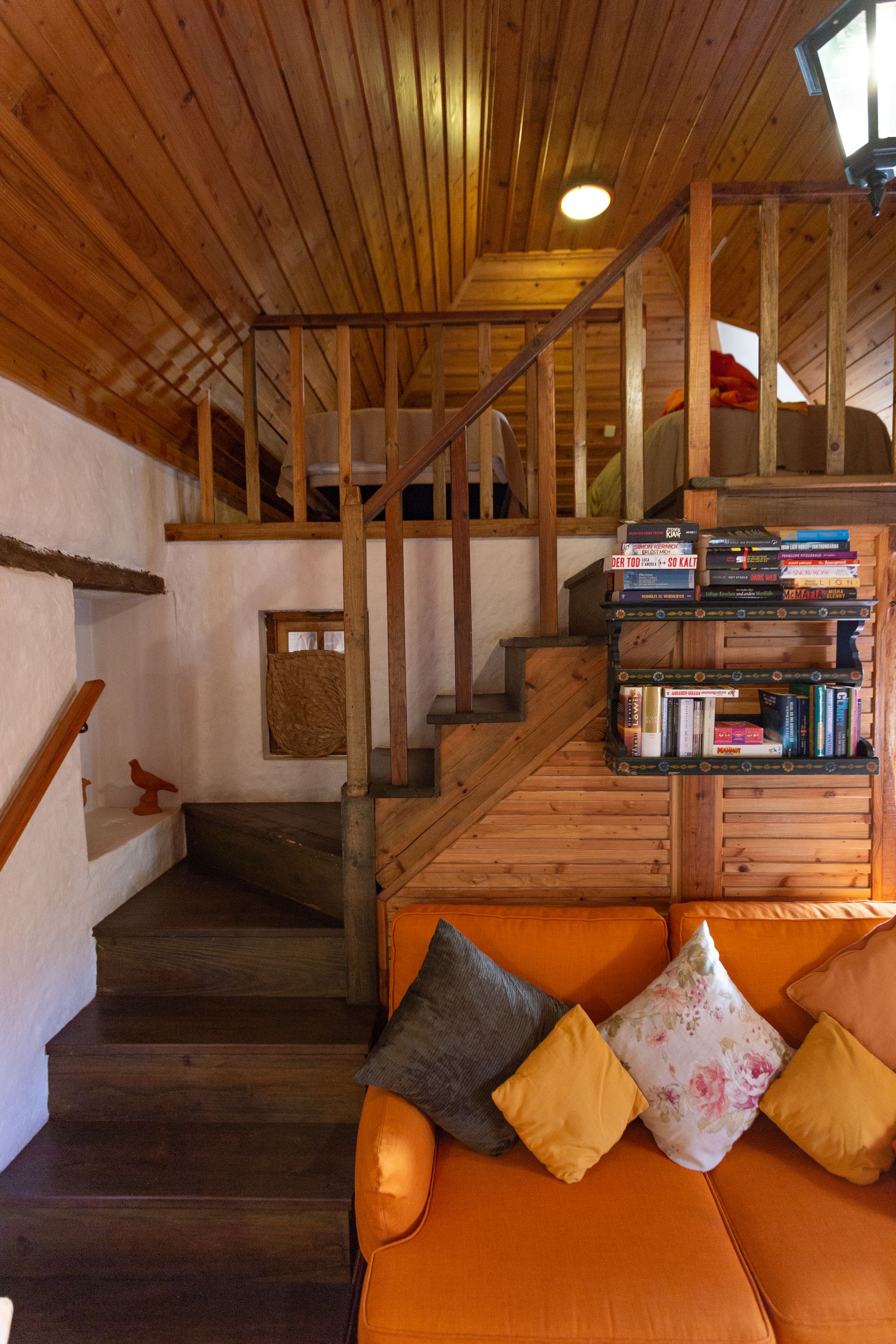 Cozy interior with a loft. Wooden stairs lead up to a seating area above an orange couch.
