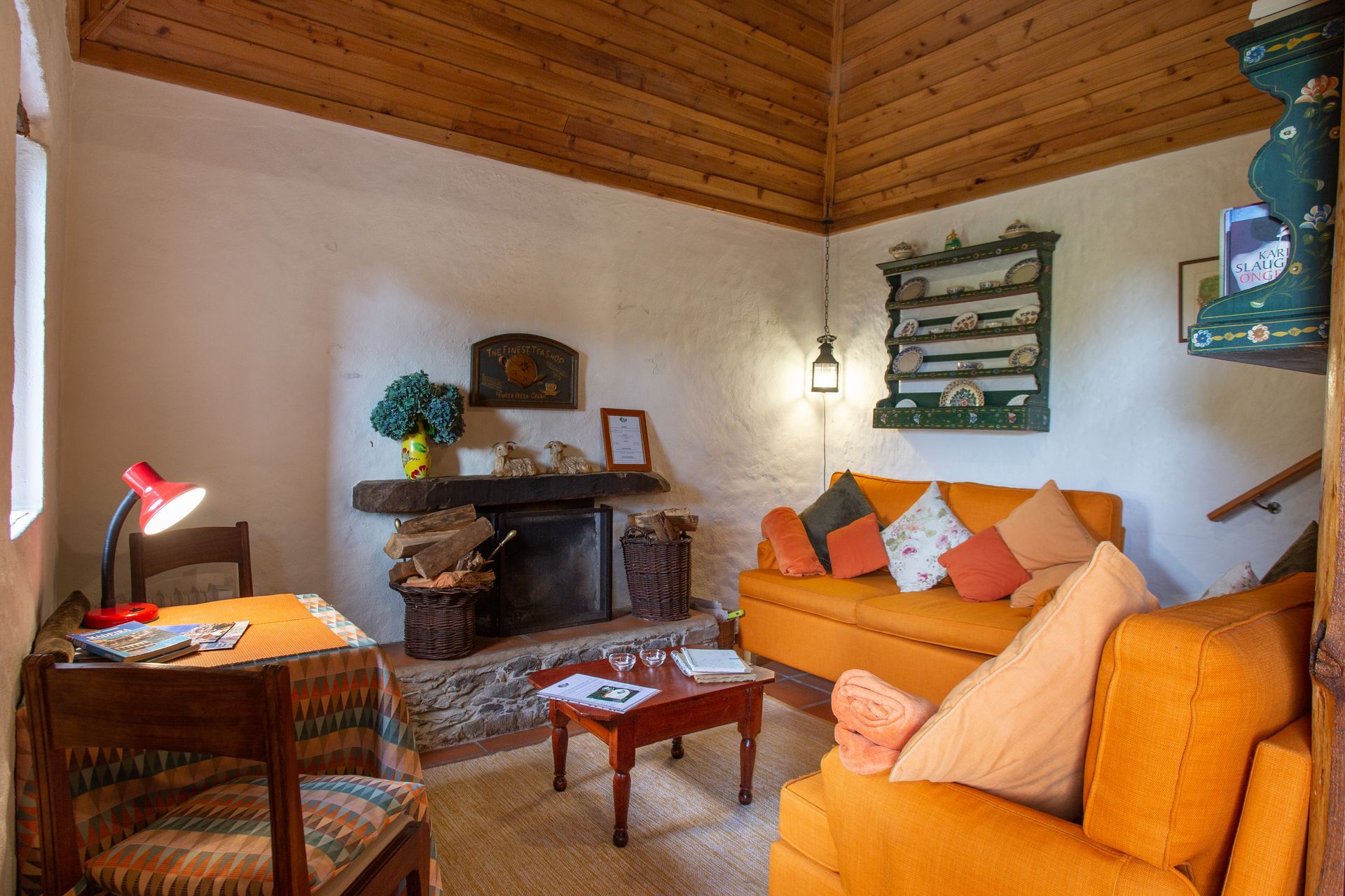 Cozy living room with orange sofa, fireplace, wooden ceiling, and desk.