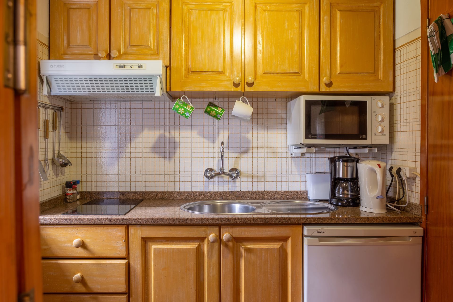 Small kitchen with wooden cabinets, microwave, and sink.