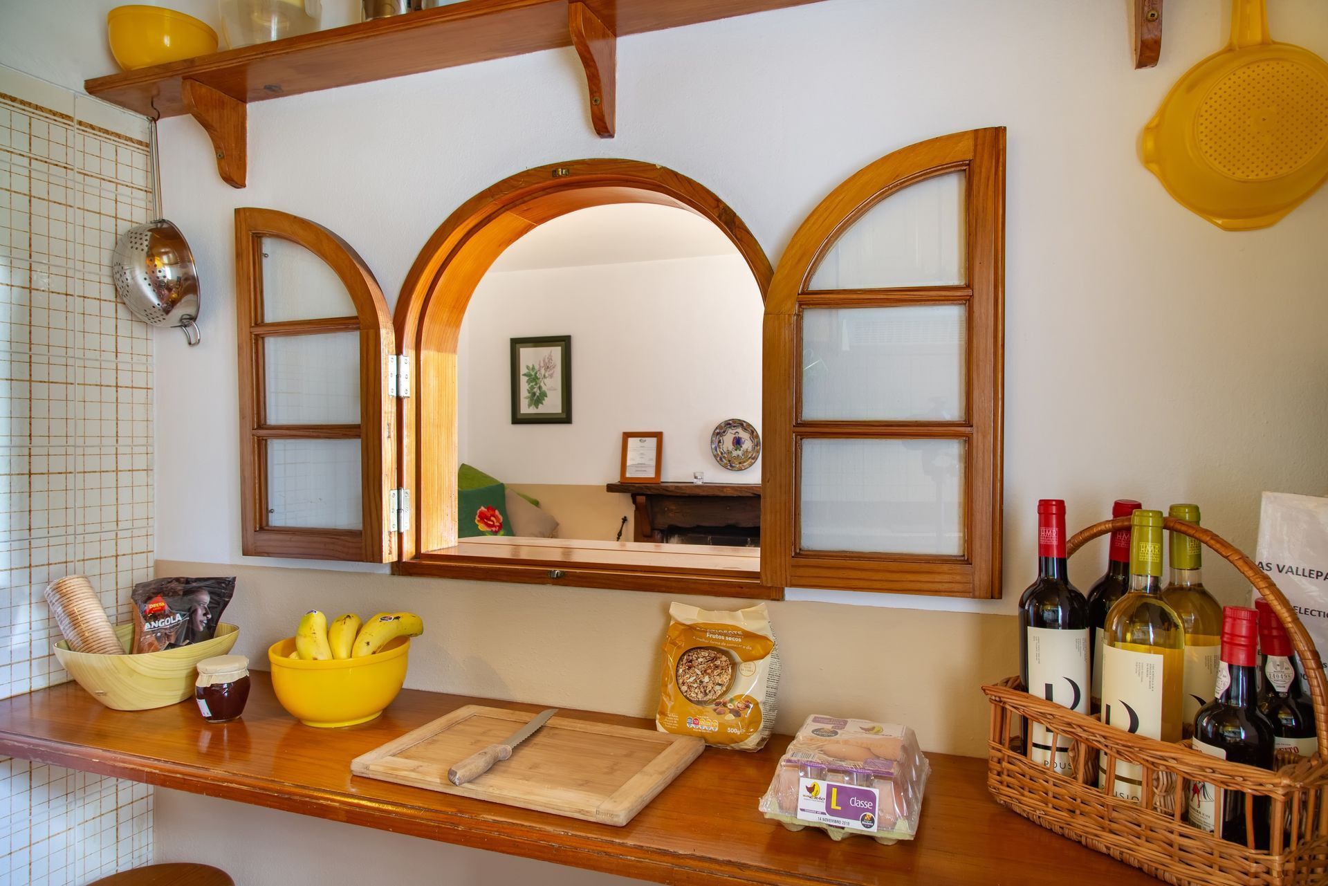 Kitchen with arched window looking into a living room, wooden countertop with food and bottles.