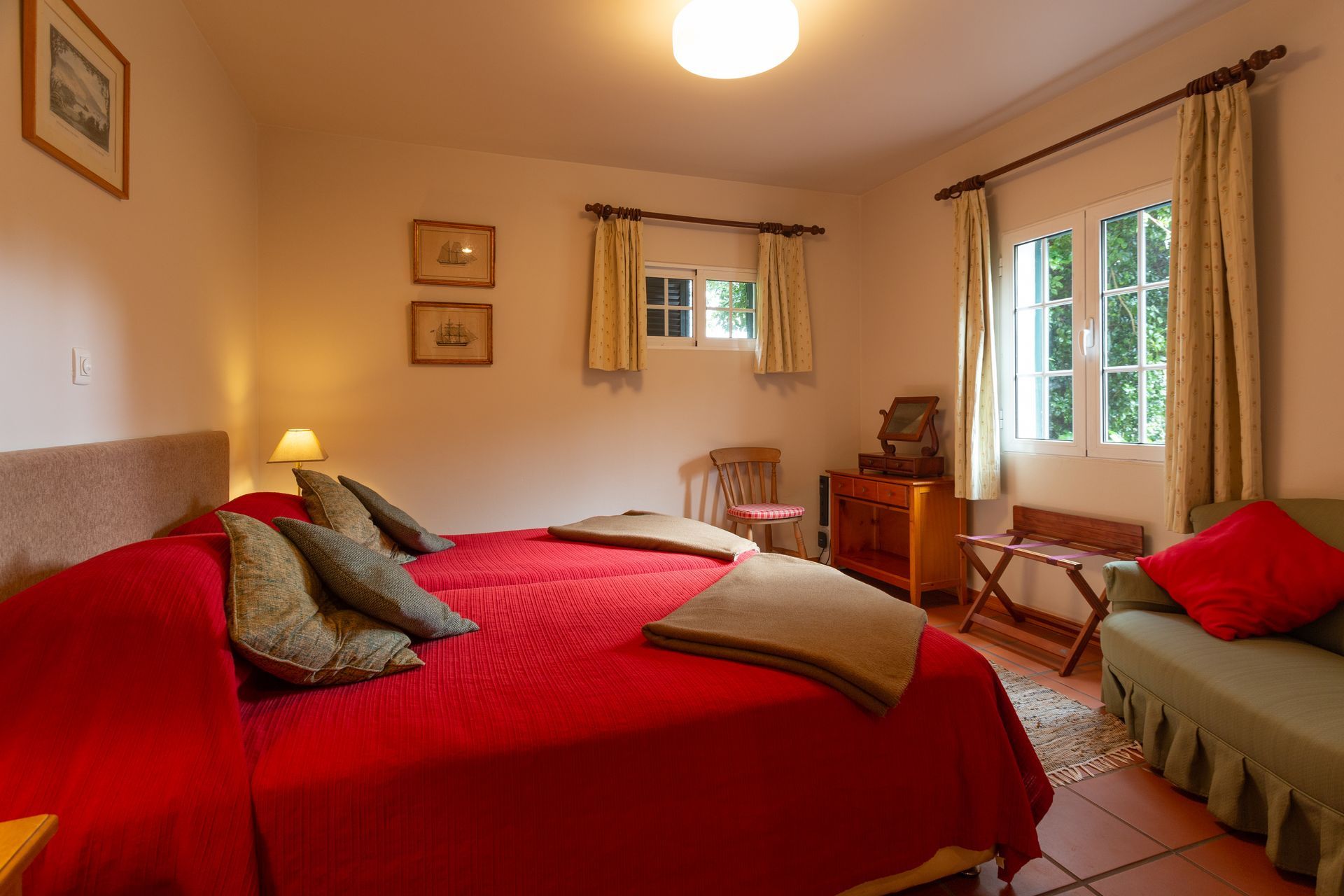 Bedroom with twin beds, red cover, and green pillows. Window, sofa, and side table present.
