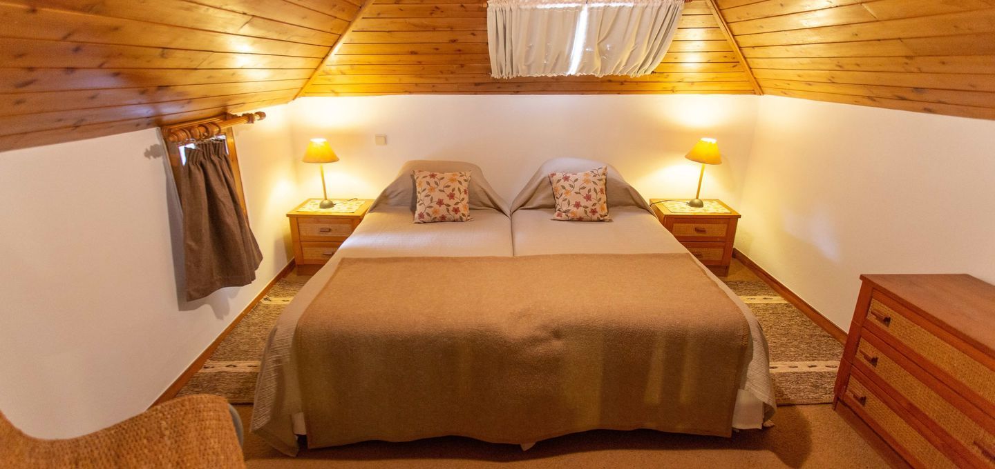 Cozy attic bedroom with a large bed, wooden ceiling, and side tables with lamps.