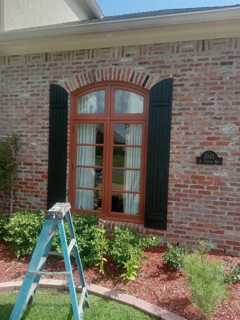 Brick house with a wooden window, black shutters, and a blue ladder.