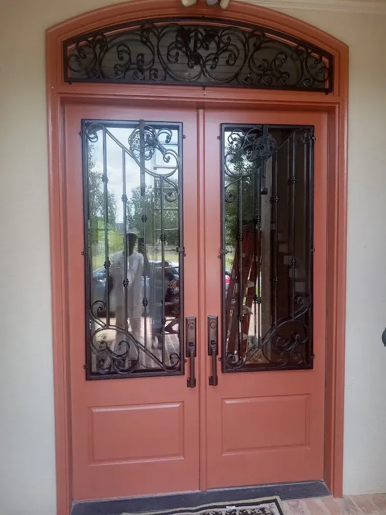 Double coral doors with black ironwork and transom, reflecting people outside.