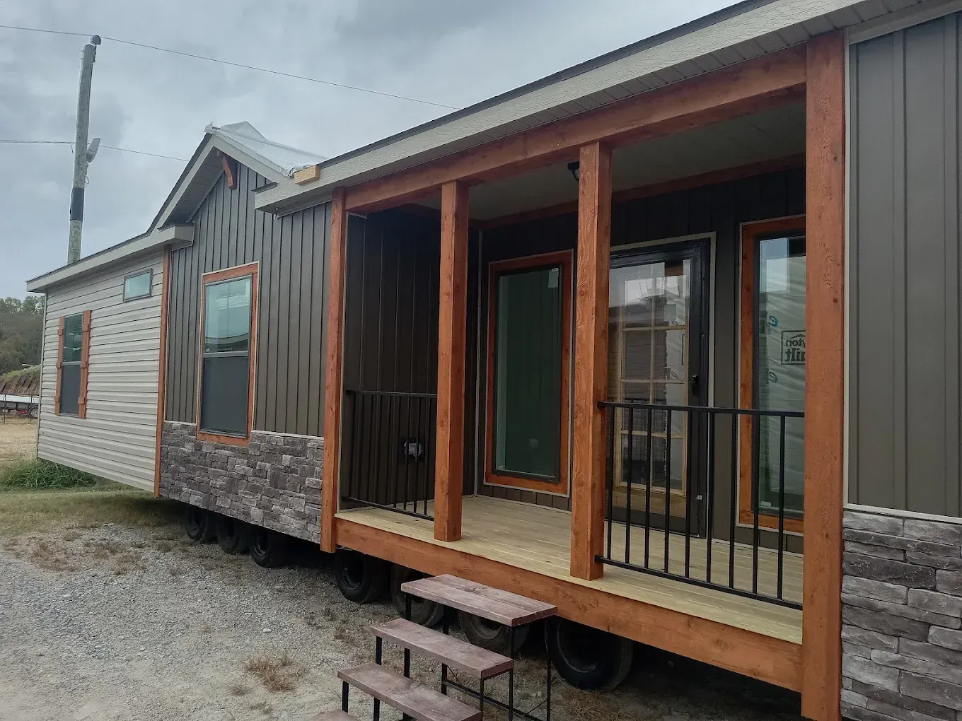A mobile home with a porch, brown siding, stone accents, and a black railing.