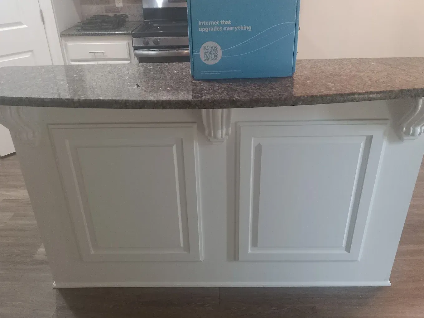 White kitchen island with dark speckled countertop; box on top, cabinets below.