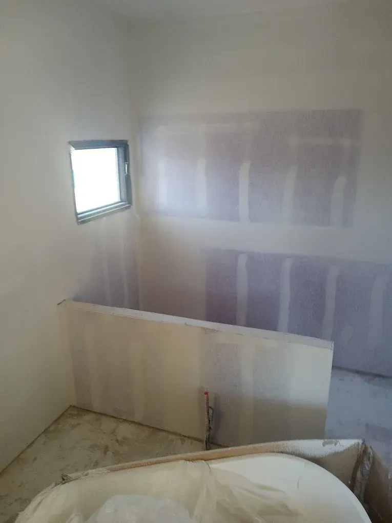 Interior construction of a small bathroom. Drywall on walls, a small window, and a tub.