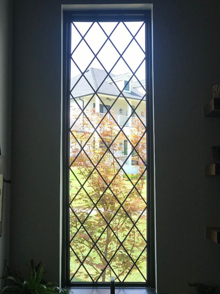 A window with a diamond pattern on it is looking out to a garden.
