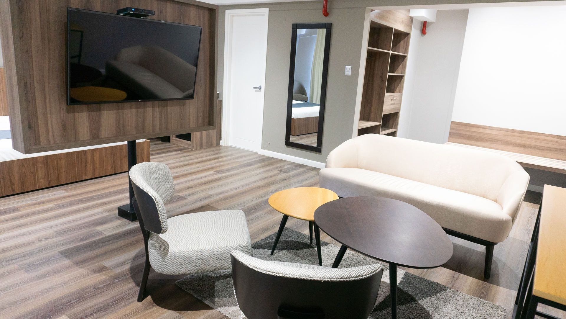 Moderna sala de estar con TV, sofá, sillas y dos mesas pequeñas sobre una alfombra.