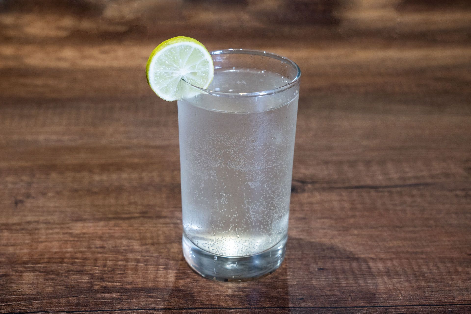 Vaso de limonada gaseosa con una rodaja de limón como decoración, colocado sobre una mesa de madera.