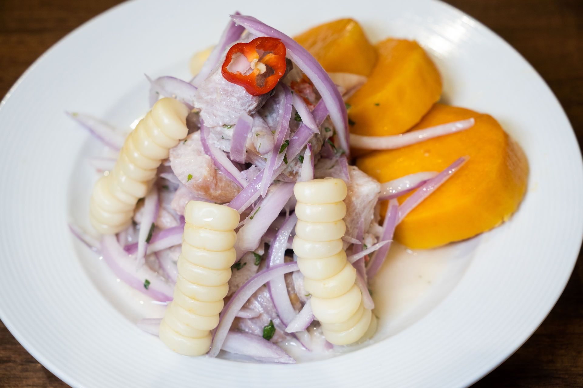Ceviche con maíz, cebolla, calabaza y chile en un plato blanco.