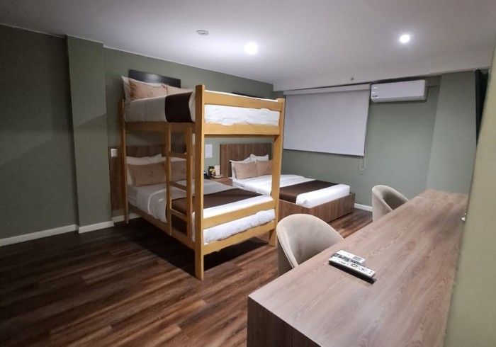 Una habitación de hotel con una litera y una cama individual con ropa de cama marrón y blanca, junto a una ventana.