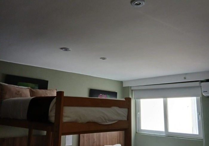 Litera en habitación con ventana y lámparas. Pared verde y techo blanco.