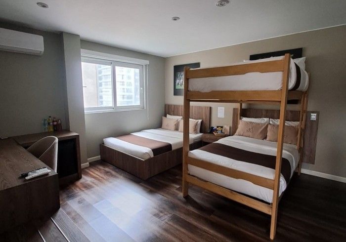 Una habitación de hotel con una litera y una cama individual, suelos de madera, escritorio y una ventana.