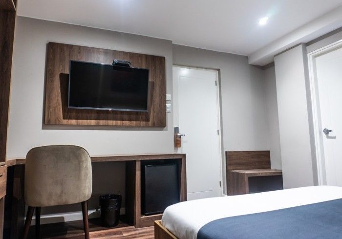 Habitación de hotel con TV, escritorio, mininevera y cama. Combinación de colores marrón y gris.