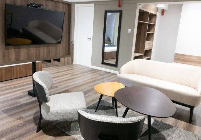 Sala de estar moderna: TV en la pared, sofá, sillas, mesas pequeñas sobre alfombra, puerta con espejo.