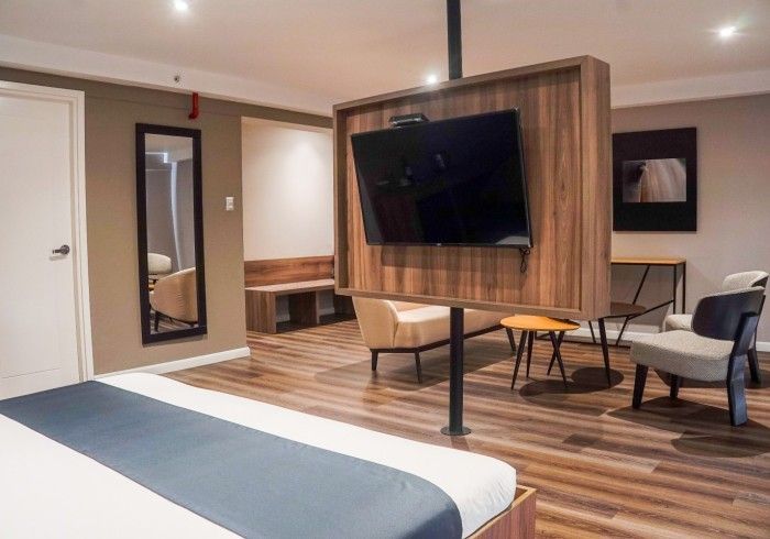 Moderna suite de hotel con una cama, TV en un poste central y zona de estar.
