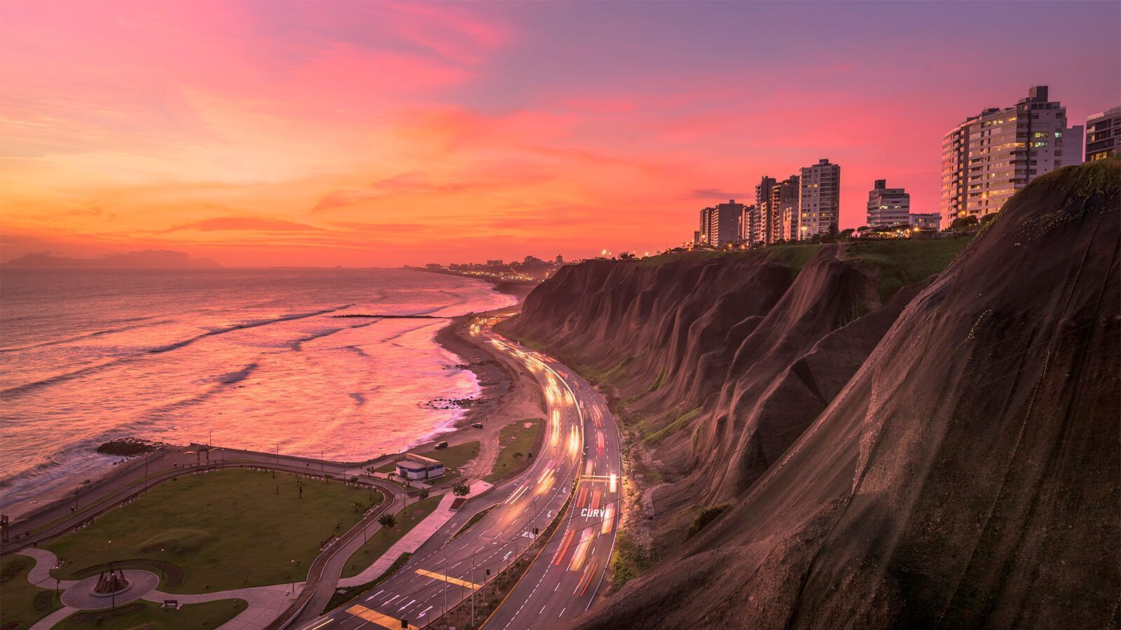 Puesta de sol sobre Lima, Perú: acantilados, océano, edificios y carretera, cielo colorido.