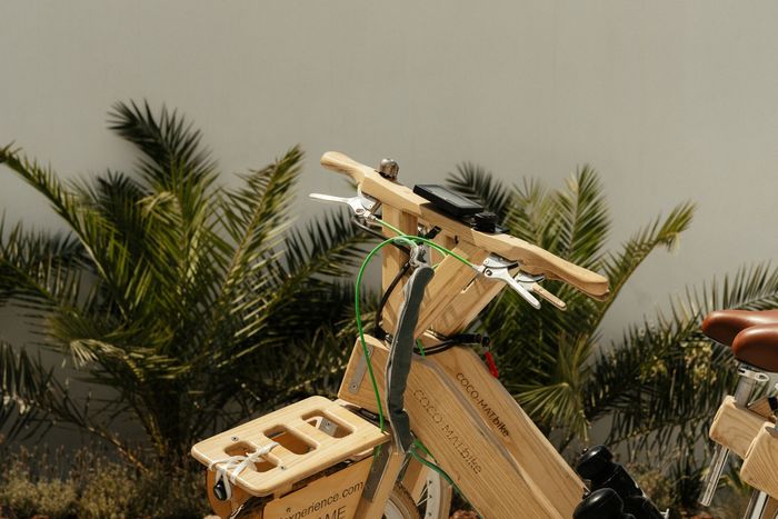 A wooden bicycle is parked in front of palm trees