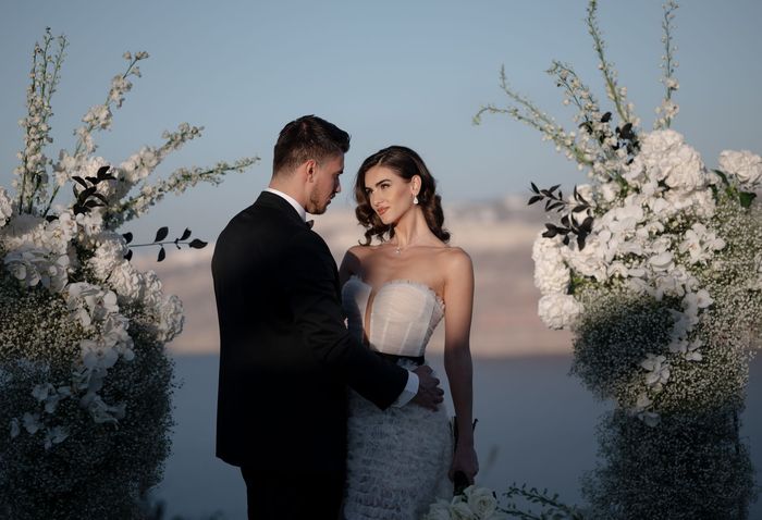 A bride and groom are standing next to each other in front of a floral arch.