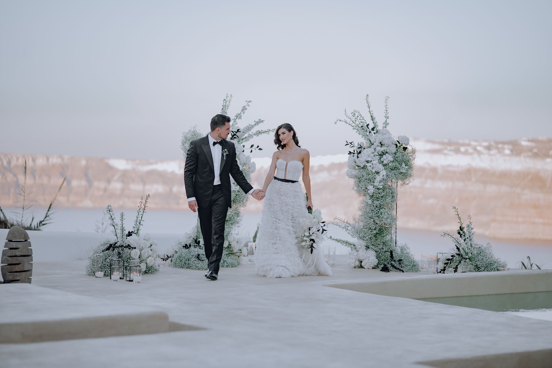 Bride and groom walking hand-in-hand outdoors, winter wedding scene with snow-covered landscape and floral arch.