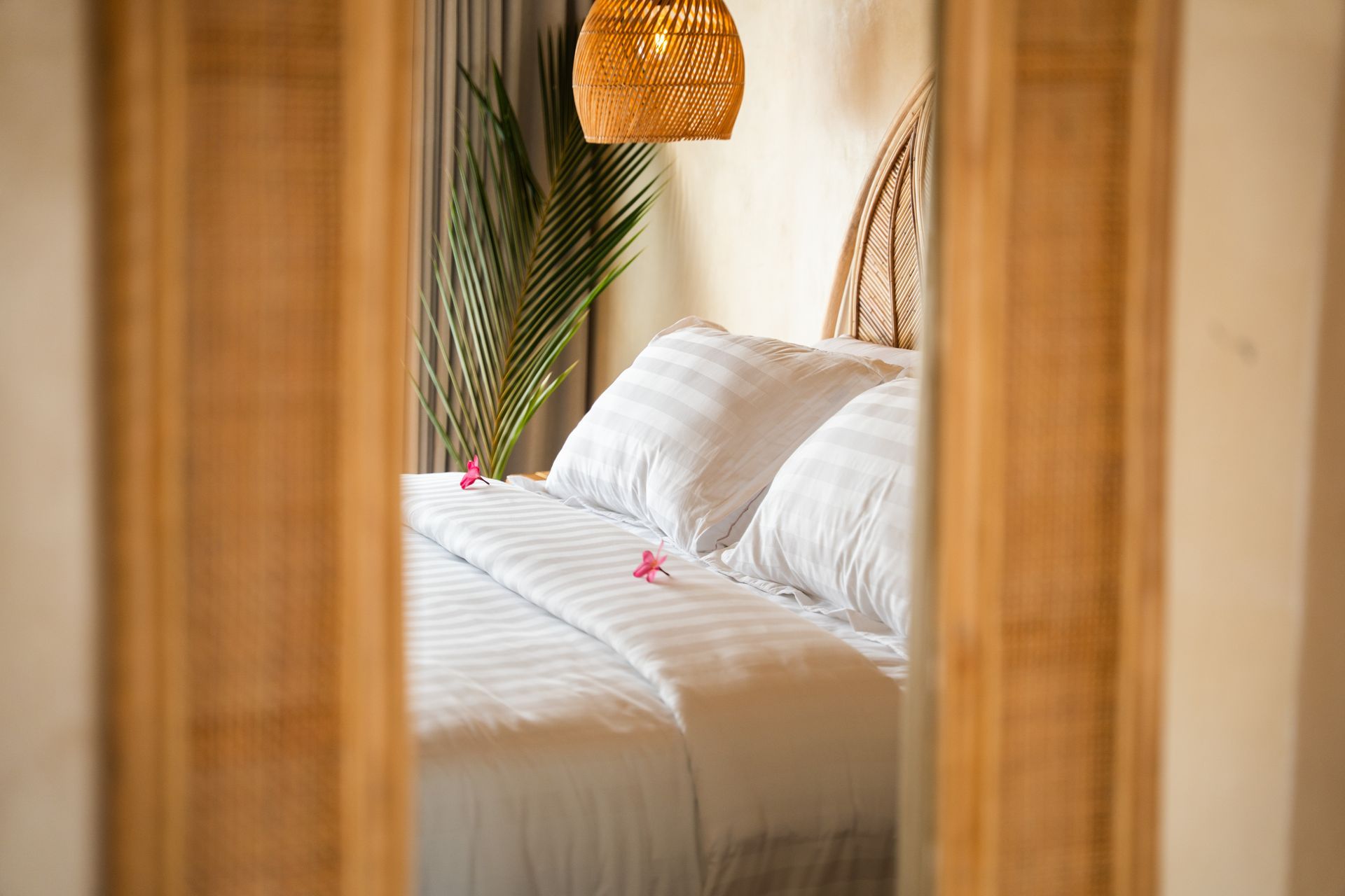 Bedroom reflected in a woven frame. White bedding, natural headboard, hanging light.