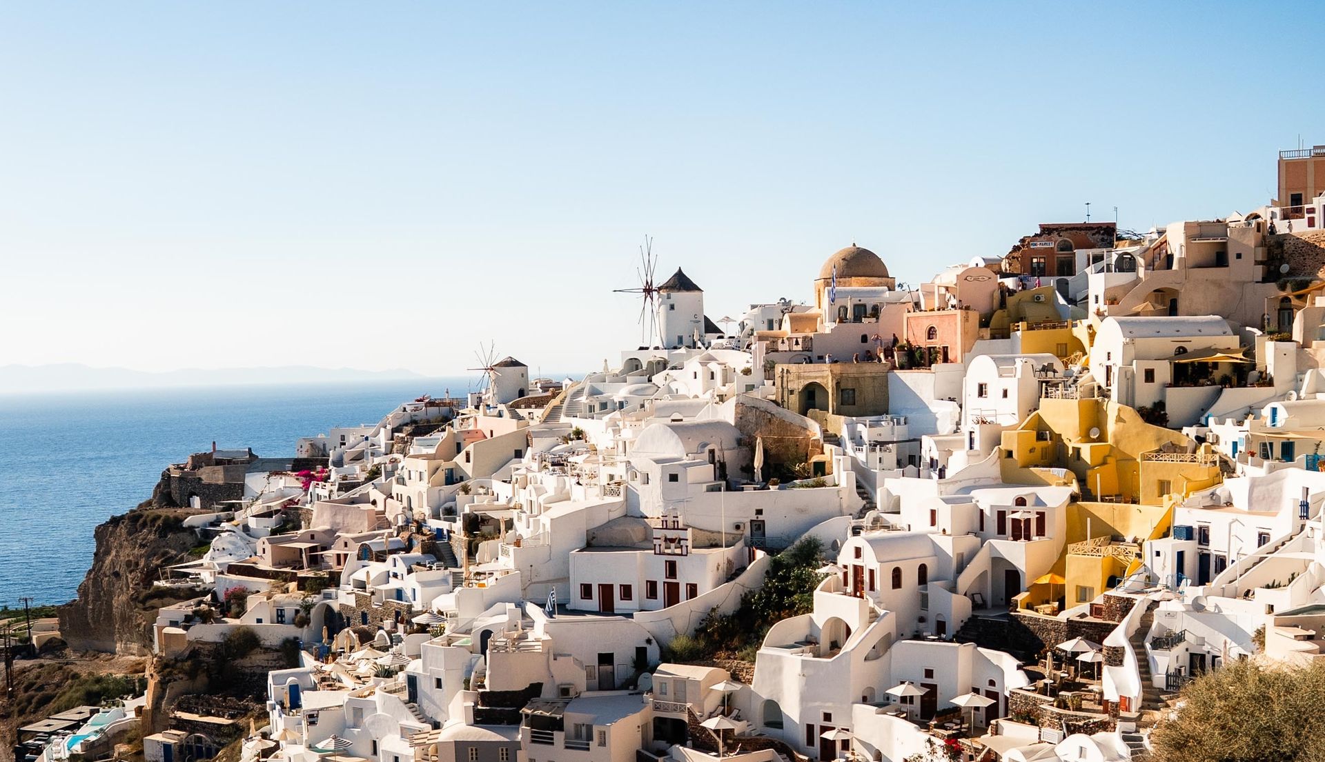 White buildings with blue domes on a cliff overlooking the blue Aegean Sea in Santorini, Greece.